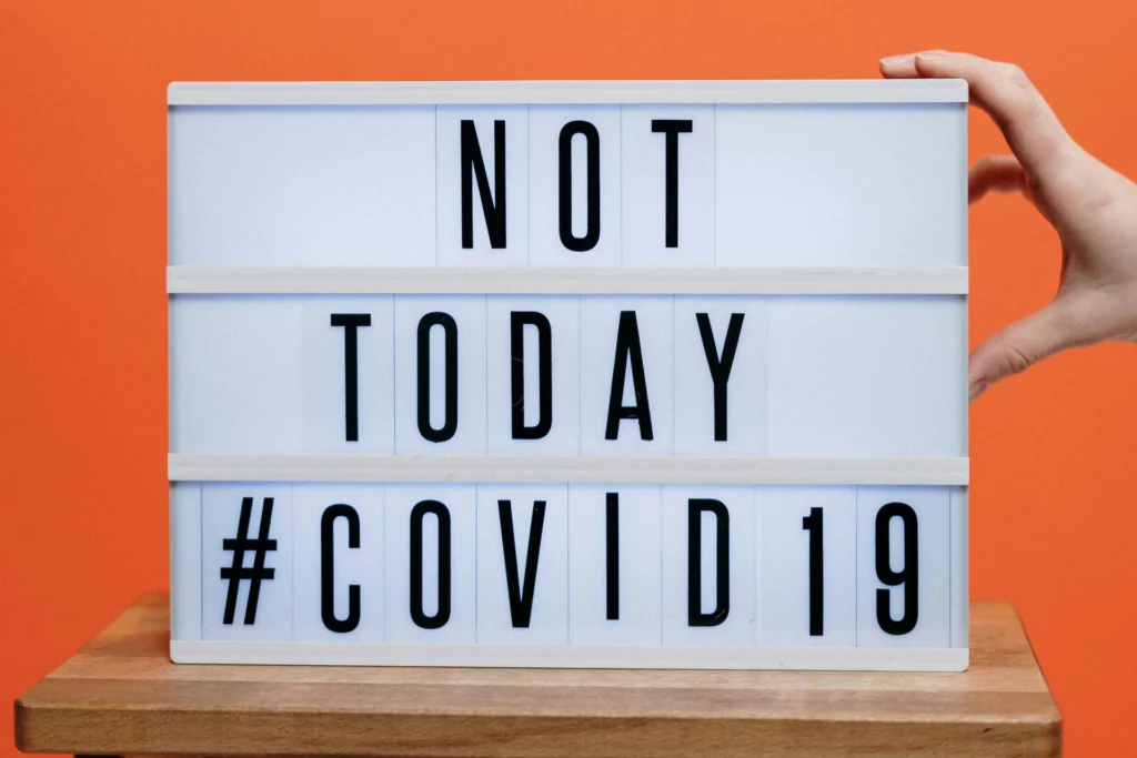 Leuchtkasten mit der Aufschrift «NOT TODAY #COVID19» vor orangefarbenem Hintergrund. Eine Hand hält die Tafel.